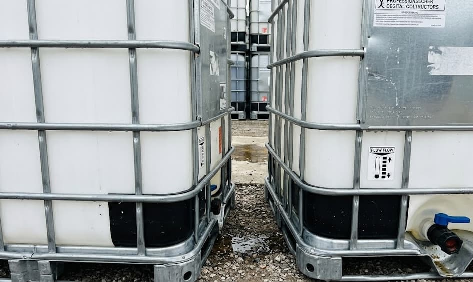 Close-up between two IBC totes showing the galvanized steel cage structure and HDPE bottle — materials that are fully recyclable in the circular economy